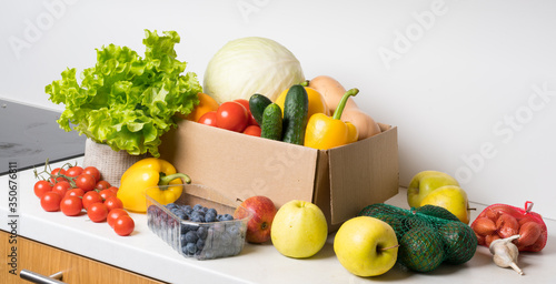 groceries box with vegetables and fruits on white kitchen background. Food delivery services during coronavirus pandemic and social distancing. Shopping online.