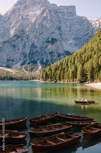 Wedding couple sailing in a wooden boat at the Lago di Braies in Italy. Newlyweds in Europe  on Braies lake  in the Dolomites. The groom rows the oars  the bride sits opposite him.