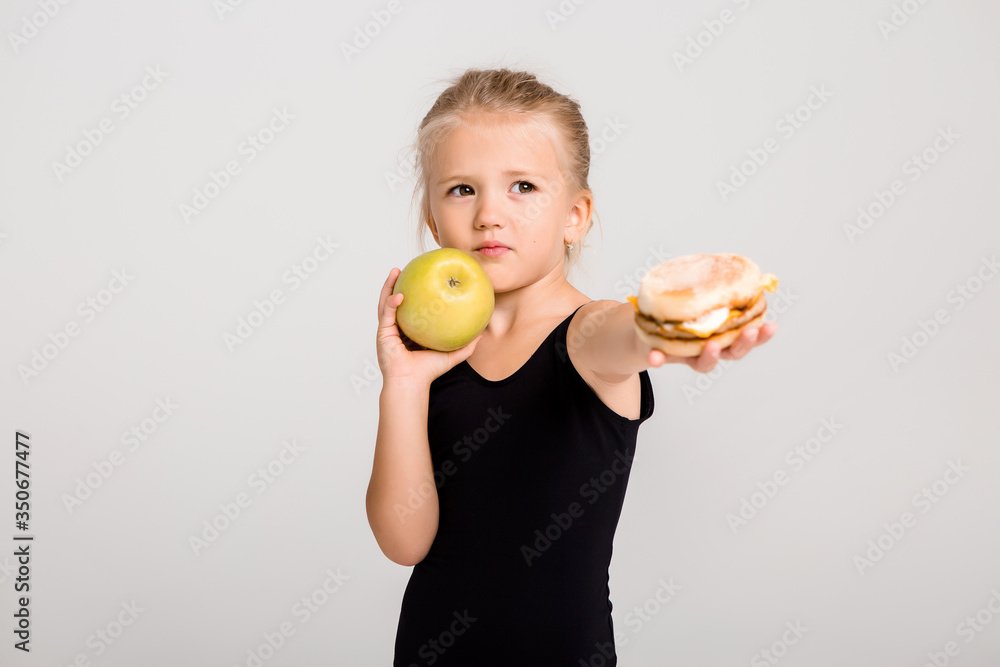 Children girl smiling holds an apple and a hamburger. Choosing healthy food, no fast food, space for text Children girl smiling holds an apple and a hamburger. Choosing healthy food, no fast food, space for text