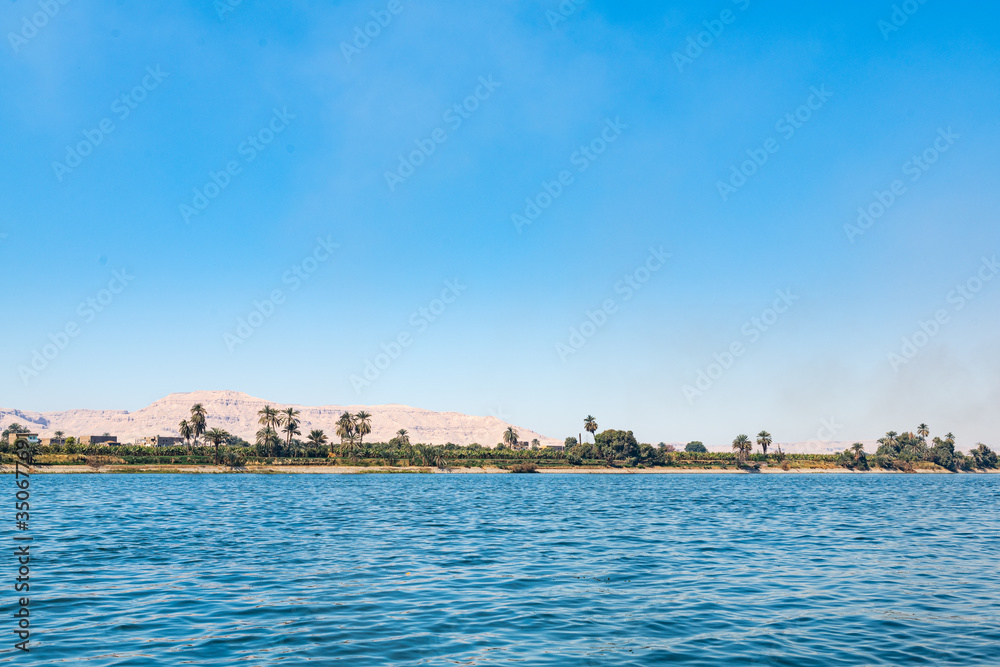 Scenic view of Nile river with palm trees on shore and limestone dunes at background