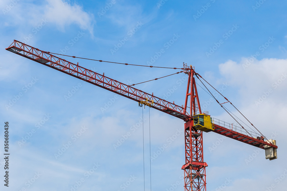  Red tower crane against blue sky with white clouds. Close up. Copy space.