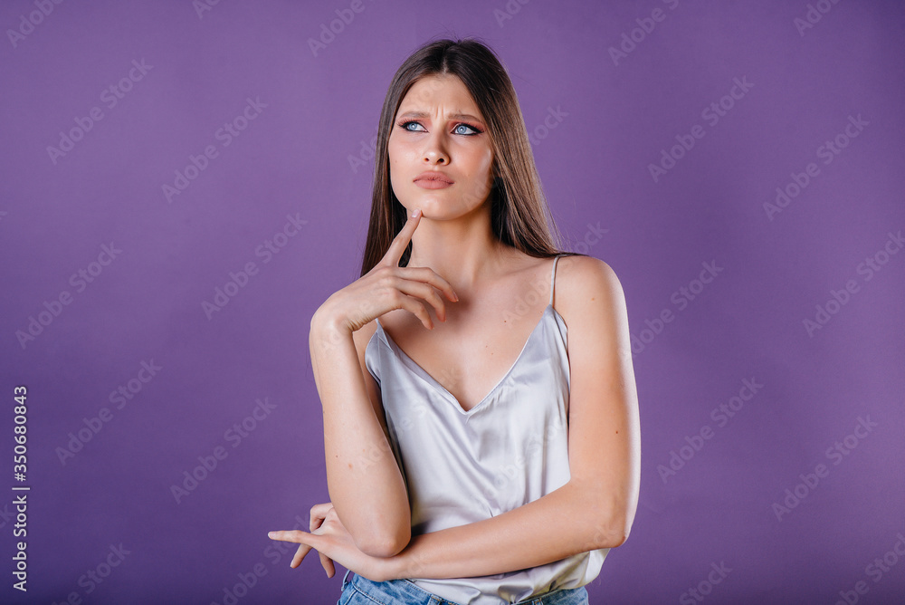 Obraz premium A young beautiful girl shows emotions and smiles in the Studio on a purple background. Girls for advertising