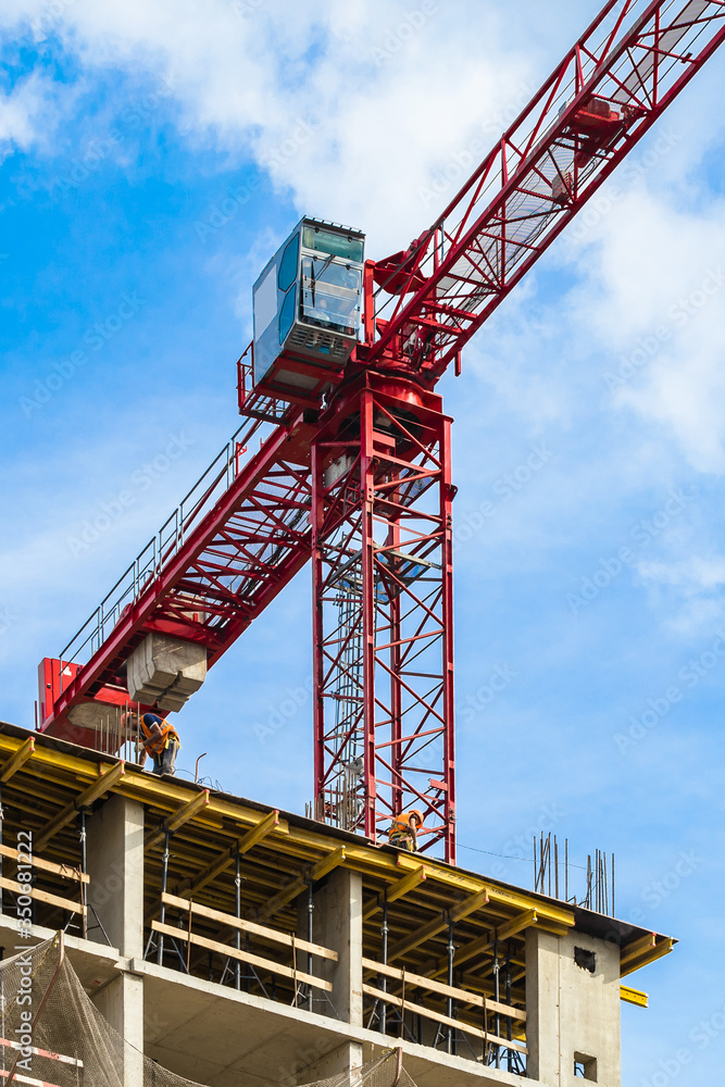 One high-rise crane with cab for man against a house and sky during the construction phase. Industry concept for low-income young families. Mortgage, business, real estate loan.