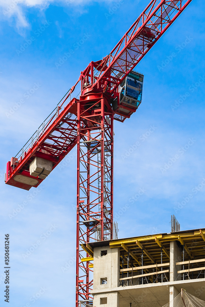 One high-rise crane against a house and sky during the construction phase. Industry concept for low-income young families. Mortgage, business, real estate loan. Outdoor.