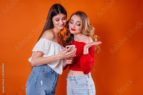 Two young and beautiful girls take a selfie and watch the phone in the Studio on a purple background. Girls for advertising