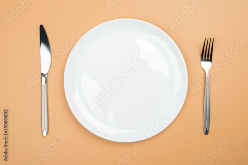 White round plate with a knife and fork on a beige background. Place for copyspace on a plate.