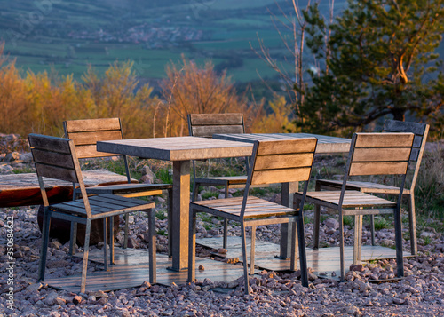 Set of tables and chairs made from metal and wood situated in the nature with trees in the background.