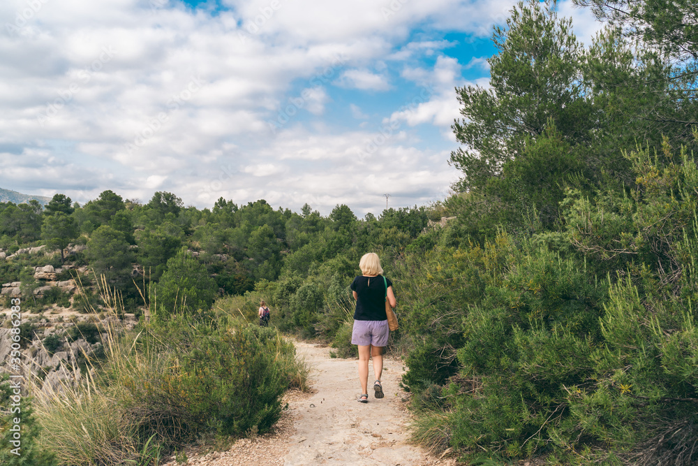 View from behind, woman on a trail, going hiking.   View of a stone path at Spanish hills,  dramatic clouds. Mediterranean green landscape.