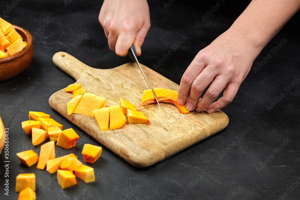 Person cutting a pumpkin on wooden chopping board on black table
