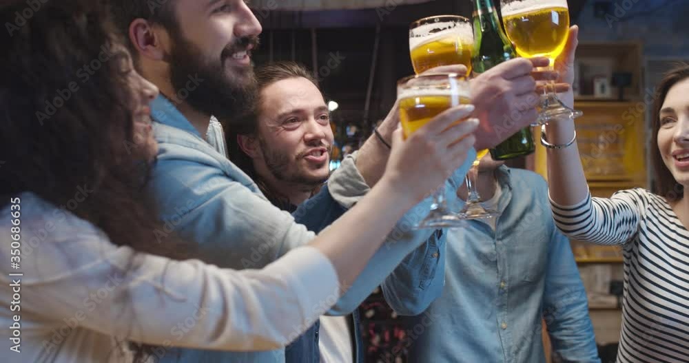 Caucasian guys and girls doing cheers gesture with beer in pub in ...