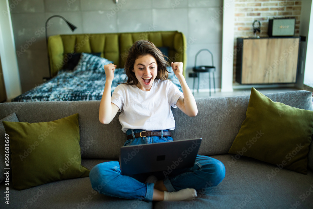 Joyful woman with win gesture using laptop on the sofa Joyful woman with win gesture using laptop on the sofa