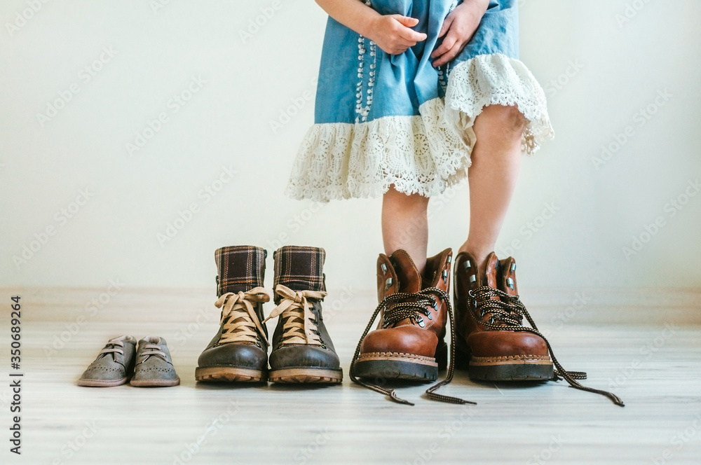 Close up of little girl in dress putting on fathers hiking shoes