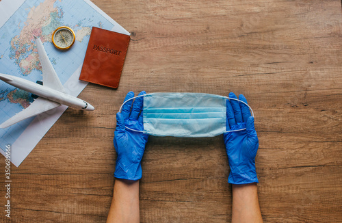 Female hands in disposable gloves holding face mask on wooden background