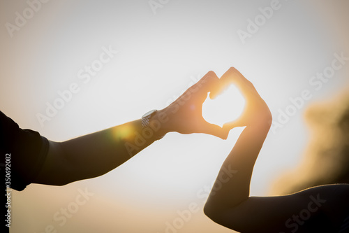 Two couple of hands form a heart at sunset