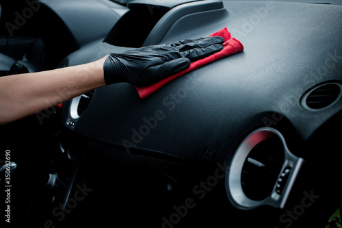 Technician with gloves cleaning the car dashboard with red cloth. Topical car wash and care. protection of the interior of the automobile. cleaning, health and care concept.