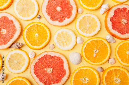 Flat lay slices of orange, grapefruit and lemon with shells on a yellow background. Summer citrus pattern