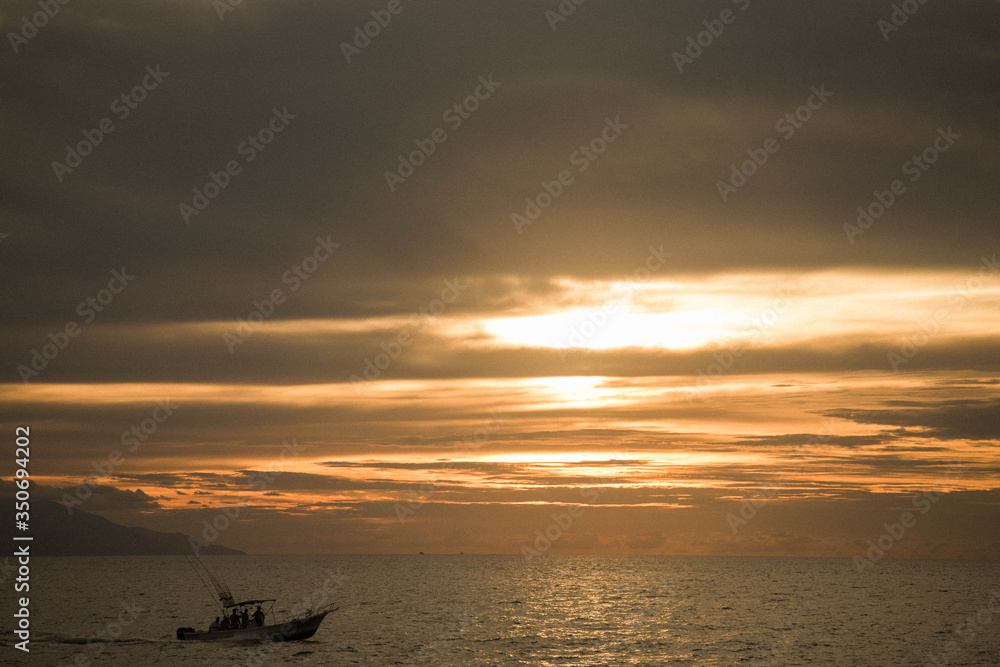 sunset over the sea in puerto Vallarta in november with a fishing boat coming back to port with their fish 