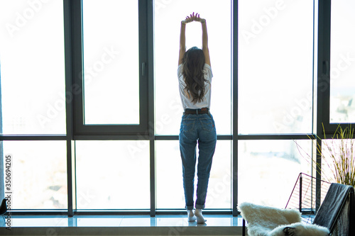 Young woman near window raising hands facing the sunrise at morning