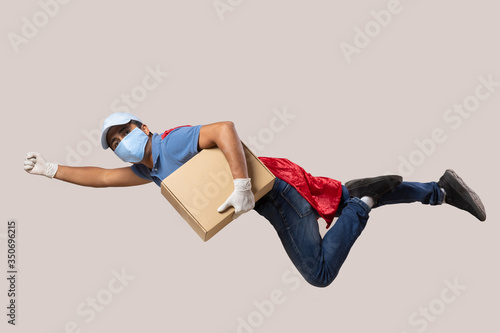 red capped courier wearing face mask and gloves due to coronavirus pandemic carrying a cardboard  box and flying 
