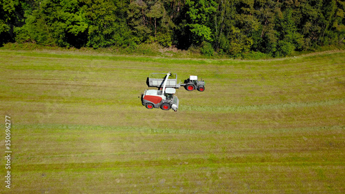 Landwirtschaft: Feldhäcksler, Traktor mit Ladewagen bei Aufnahme von Gras für Grassilage auf einer gemähten Wiese, Vogelperspektive