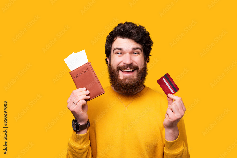 bearded man is holding his passport and some tickets he paid with card on yellow background. bearded man is holding his passport and some tickets he paid with card on yellow background.