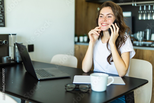 Beautiful young woman working on computer and talking on phone at home