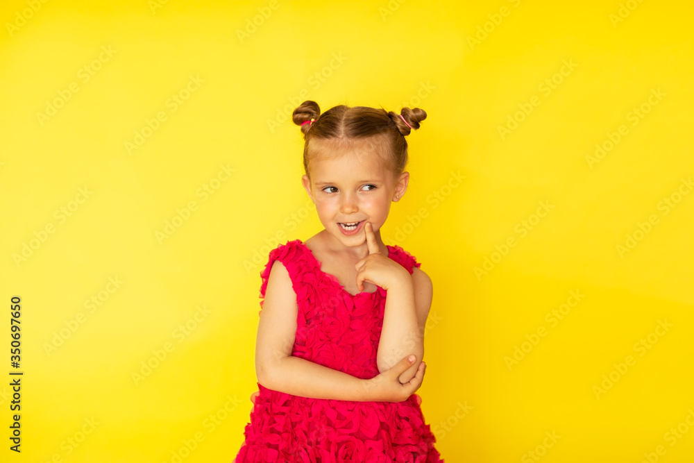 Pretty little barefooted girl with two buns and in bright pink summer dress posing with emotions on yellow background. Copy space Pretty little barefooted girl with two buns and in bright pink summer dress posing with emotions on yellow background. Copy space