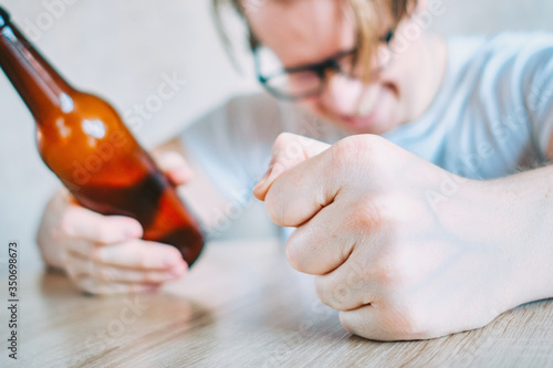 Glasses angry man drinks beer at the table.