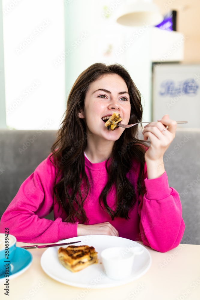 Attractive happy young woman sitting and eating dessert in cafe Attractive happy young woman sitting and eating dessert in cafe