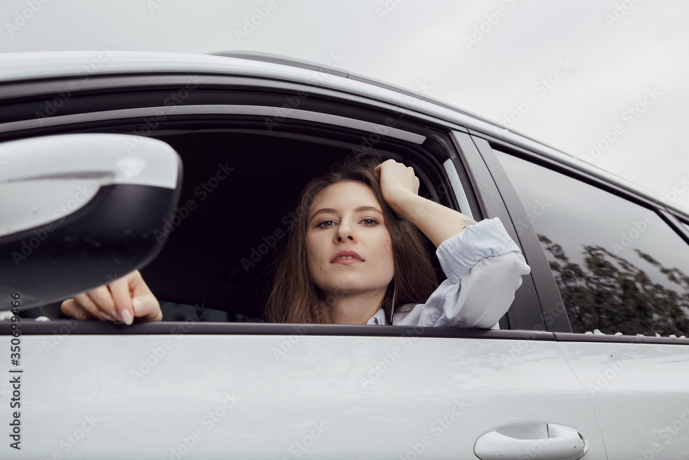 Young woman driving a car. The girl sits in the driver's seat. Young beautiful girl with a nice smile driving a car. Exterior view of the car Young woman driving a car. The girl sits in the driver's seat. Young beautiful girl with a nice smile driving a car. Exterior view of the car