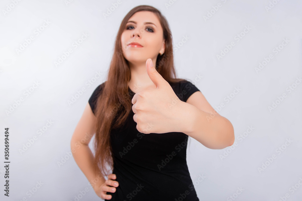 Close up focus on thumb up shot on wide angle lens. Young, attractive woman in a black t-shirt isolated on a white background shows a gesture of approval and success. Close up focus on thumb up shot on wide angle lens. Young, attractive woman in a black t-shirt isolated on a white background shows a gesture of approval and success.