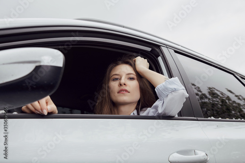 Young woman driving a car. The girl sits in the driver's seat. Young beautiful girl with a nice smile driving a car. Exterior view of the car © ibilyk13