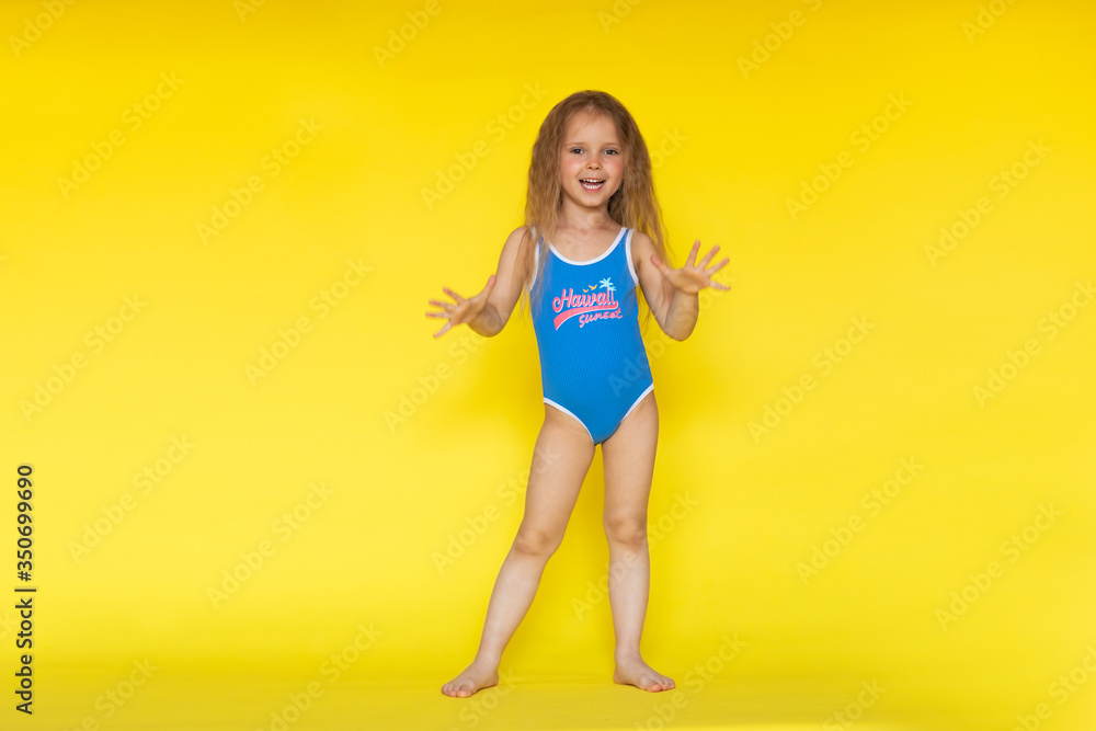 Little girl with brown hair in blue swimsuit posing on yellow background
