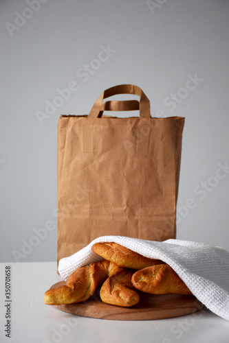 Pastry delivery of fresh bakery products, rolls under white kitchen napkin on white table and paper packaging