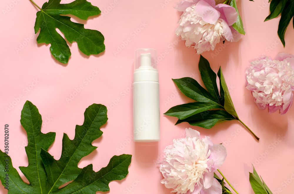 White bottle with place for your text on a pink background with flowers and leaves. Beauty concept. White bottle with place for your text on a pink background with flowers and leaves. Beauty concept.