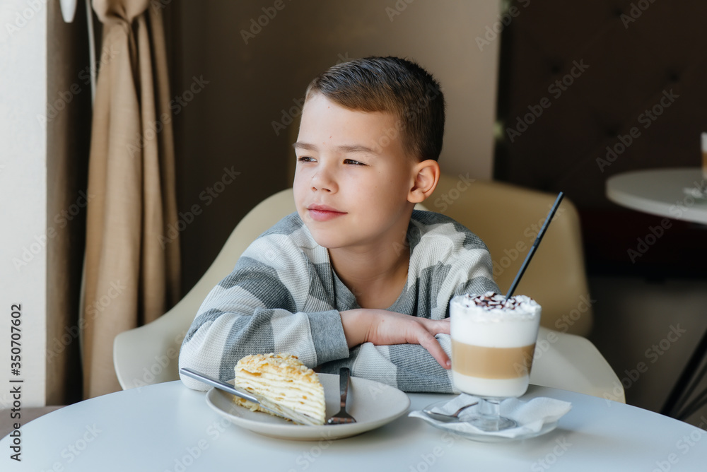 A cute little boy is sitting in a cafe and looking at a cake and cocoa close-up. Diet and proper nutrition