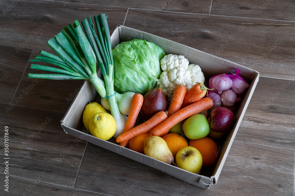 Fresh vegetables in cardboard box on brown wood background.