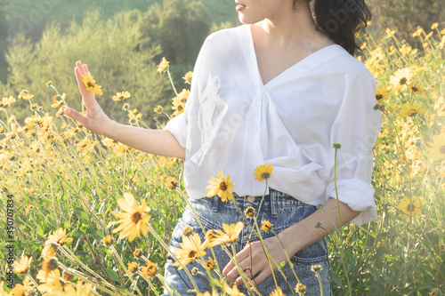 Brunette woman holding yellow daisy in flower field in the sunlight photo