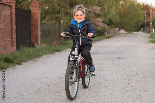 Young boy riding on bicycle with face mask due to pandemic Covid-19.