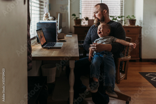 Father trying to work from home with toddler tantrum in his lap