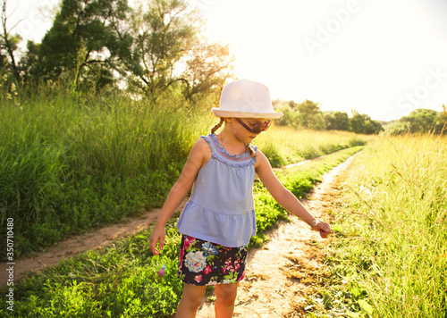 Beautiful fun kid girl walking on the path and enjoying green grass summer sunny background. Closeup © nastia1983