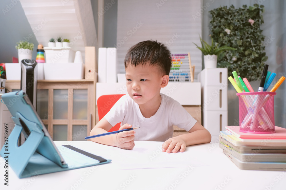 Asian schoolboy kid using tablet pc computer studying homework during his online lesson at home, Kindergarten closed during the Covid-19 health crisis, Distance learning, homeschooling concept Asian schoolboy kid using tablet pc computer studying homework during his online lesson at home, Kindergarten closed during the Covid-19 health crisis, Distance learning, homeschooling concept