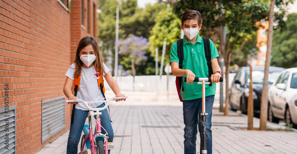 Boy and girl wearing masks and riding a scooter and bicycle on street