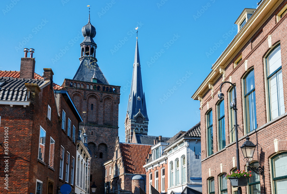 Fototapeta premium Culemborg centre with houses at the Varkensmarkt (Pigs Market Square), the Binnenpoort (Town Gate) tower and the St. Barbara church tower on a sunny afternoon. Gelderland, The Netherlands.