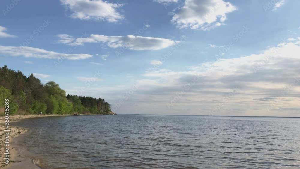 Shore with green trees and white sand, water with sun flare and waves, blue sky Shore with green trees and white sand, water with sun flare and waves, blue sky