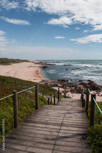 A wooden staircase leading to the white sand beach. Landscape  panorama of the ocean  beach and coastline  green grass. 