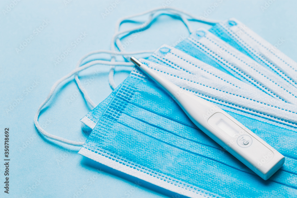One white digital thermometer on top of some blue face masks One white digital thermometer on top of some blue face masks