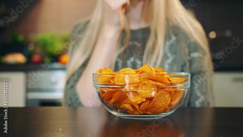 Glad woman eating potato chips. Beautiful young female enjoying potato chips and looking at camera while sitting in stylish kitchen.