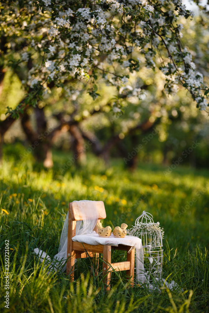 Vintage children' Decore in spring blooming apple garden. Wooden children chair in the garden, outdoor decorative composition decorative cell with flowers & ceramic birds. Spring blossom - obrazy, fototapety, plakaty 