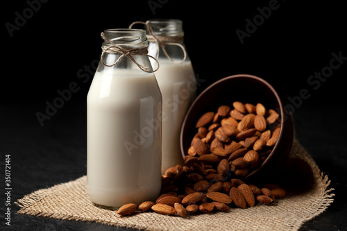 almond milk in glass bottles on a black background with nuts, vegetarian milk without sugar and lactose